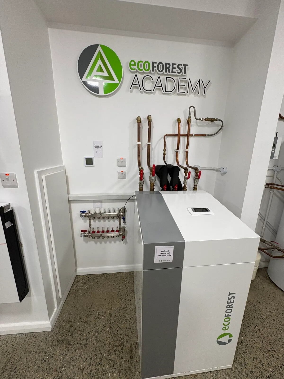 Ecoforest geothermal heat pump unit and heating manifold under the Ecoforest Academy sign in the EHP showroom